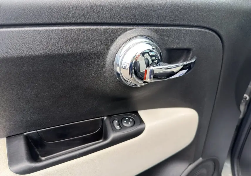 Poignée de porte intérieure chromée côté conducteur avec panneau noir et beige sur Fiat 500 gris foncé 2020.