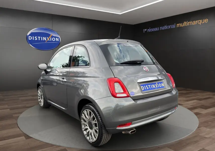 Fiat 500 gris foncé vue 3/4 arrière droit, avec jantes alliage et sortie d’échappement chromée visible.