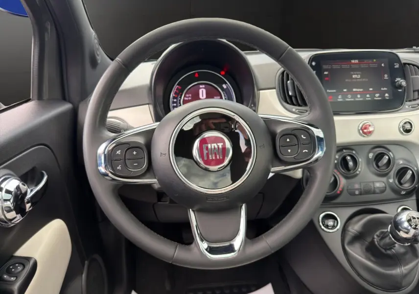 Vue intérieure centrée sur le volant cuir multifonctions d'une Fiat 500 2020 avec tableau de bord et écran tactile.