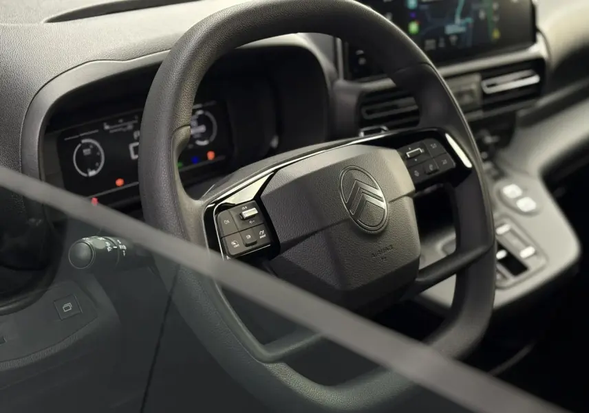 Vue rapprochée du volant multifonctions noir du Citroën Berlingo 2025 avec tableau de bord numérique en arrière-plan.