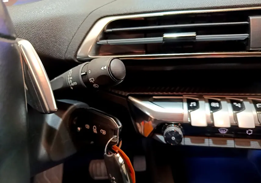 Gros plan sur la commande d'essuie-glace et la clé insérée côté gauche du tableau de bord noir du Peugeot 3008 blanc 2020.