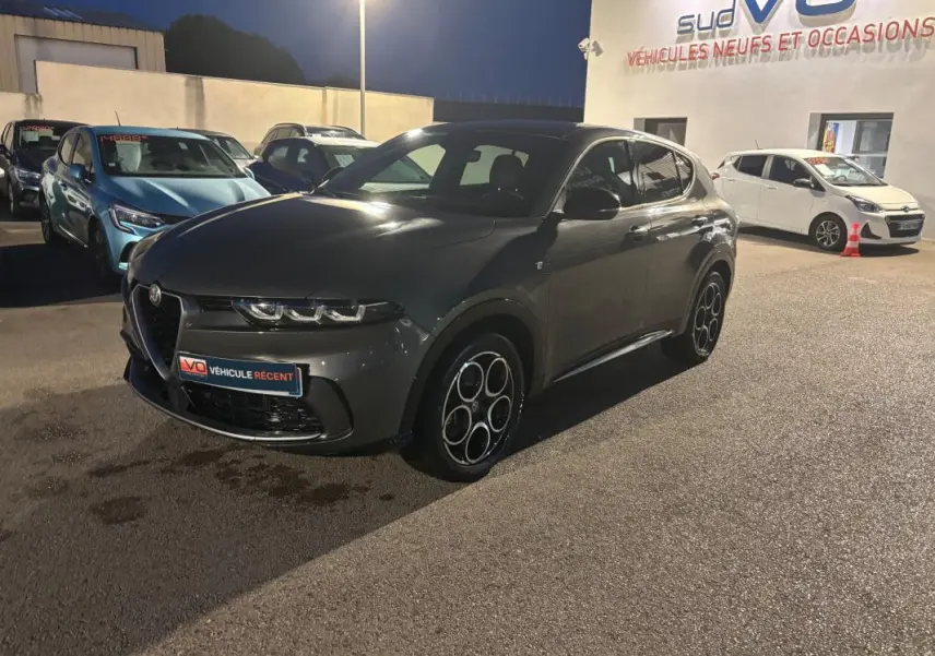 Vue 3/4 avant d'une Alfa Romeo Tonale gris métallisé avec jantes alliage 18 pouces, stationnée de nuit en extérieur.