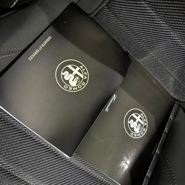 Vue intérieure rapprochée sur siège en tissu gris avec deux manuels Alfa Romeo Tonale posés, soulignant l'ambiance sobre.