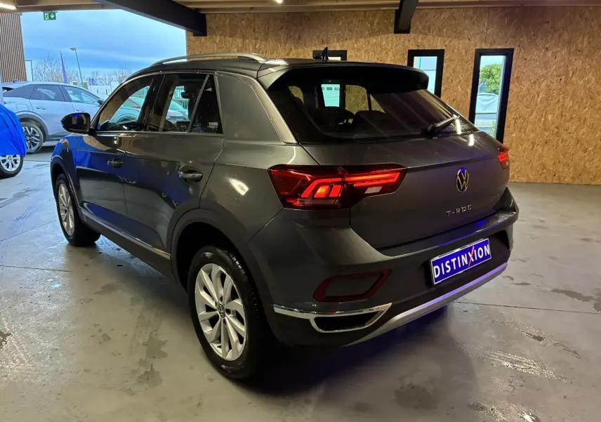 Vue 3/4 arrière droite d'un Volkswagen T-Roc gris 2023 avec feux arrière allumés dans un garage.