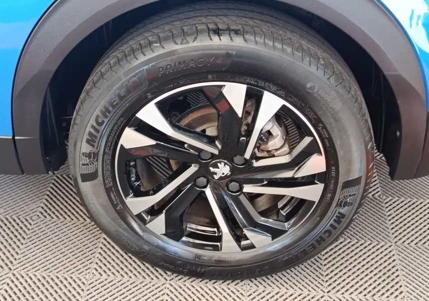 Gros plan sur la roue avant droite d’un Peugeot 2008 bleu avec jante alliage noire et argentée au design moderne.