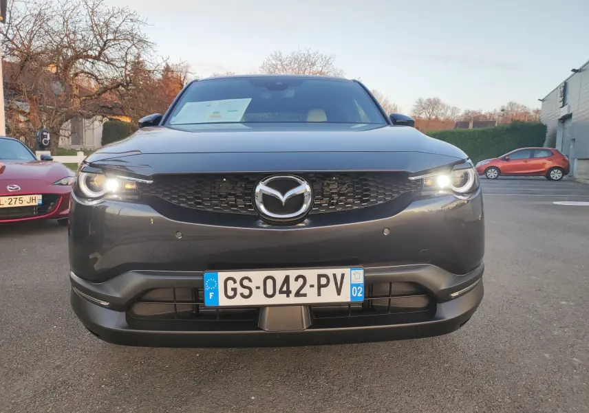 Vue frontale d'une Mazda MX-30 gris foncé 2023 avec phares allumés et calandre noire distinctive.