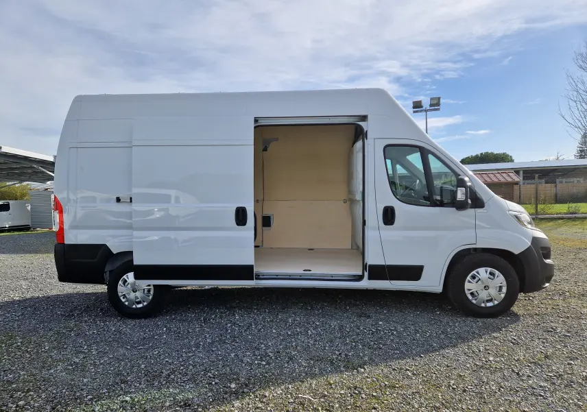 Vue latérale droite d'un utilitaire blanc Citroën Jumper L3H3 2023 avec porte coulissante ouverte montrant l'intérieur en bois.
