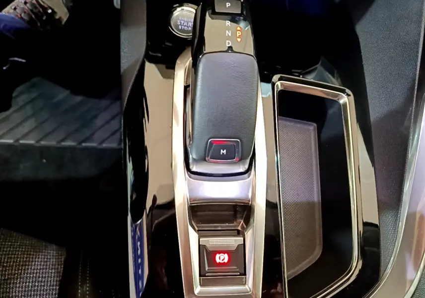 Gros plan sur la console centrale de la Peugeot 5008 gris clair, avec levier de vitesse automatique et frein à main électrique.