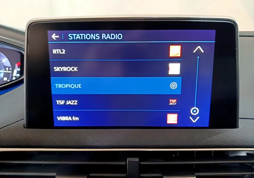 Écran tactile central affichant les stations radio dans l’habitacle d’un Peugeot 5008 gris clair, vue frontale rapprochée.