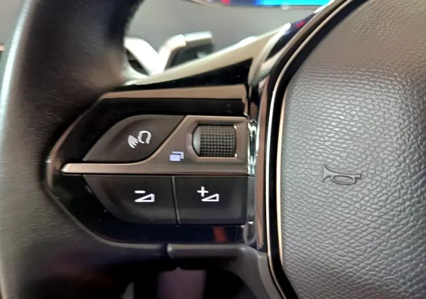 Gros plan sur les commandes gauche du volant cuir du Peugeot 5008 gris clair, avec boutons multifonctions et molette tactile.