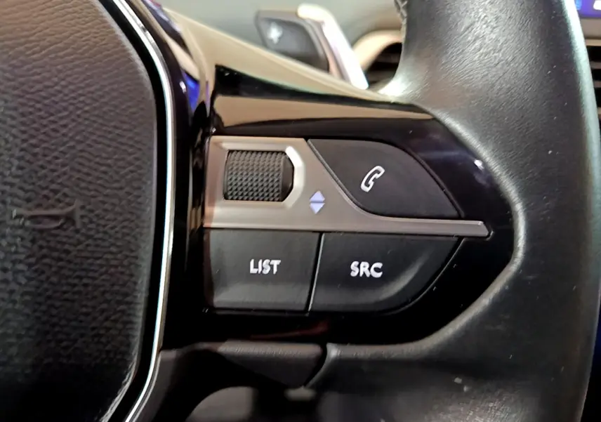 Gros plan sur les commandes gauche du volant cuir noir du Peugeot 5008 gris clair, boutons LIST, SRC et téléphone visible.