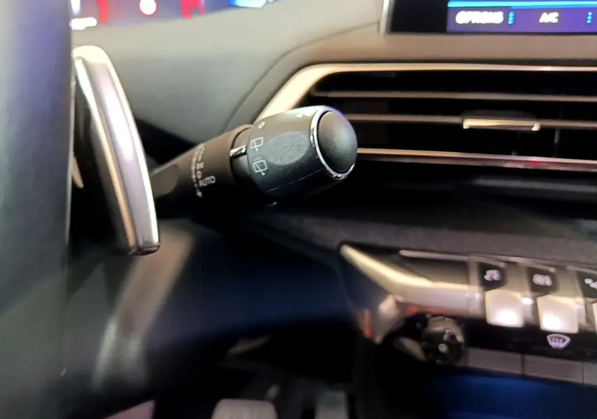Gros plan sur la commande d'essuie-glace à gauche du volant dans l'habitacle sombre du Peugeot 5008 gris clair.