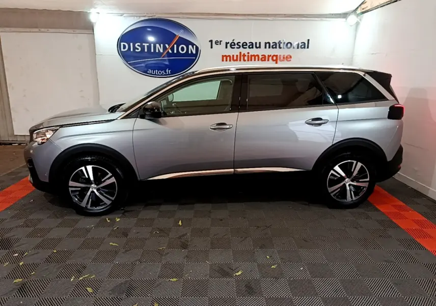 Vue de profil côté gauche d'un Peugeot 5008 gris clair stationné en intérieur avec jantes alliage et vitres teintées.