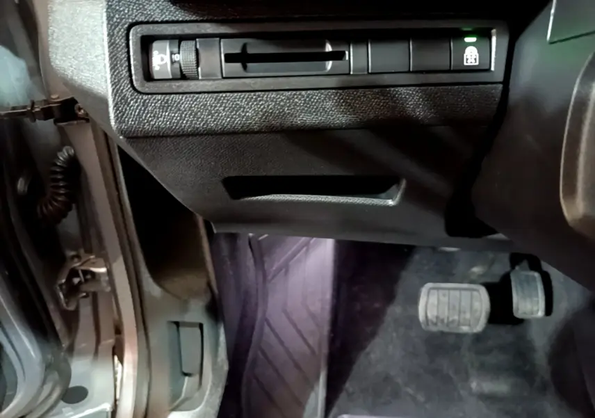 Vue intérieure côté conducteur du Peugeot 5008 gris clair, montrant les pédales et commandes sous le tableau de bord.