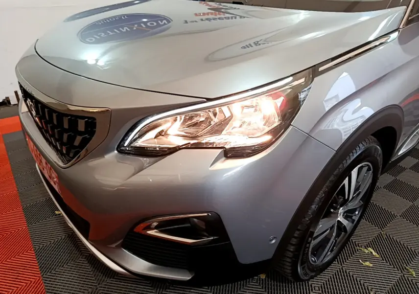 Vue 3/4 avant droit d'un Peugeot 5008 gris clair avec phares allumés et jantes alliage visibles.