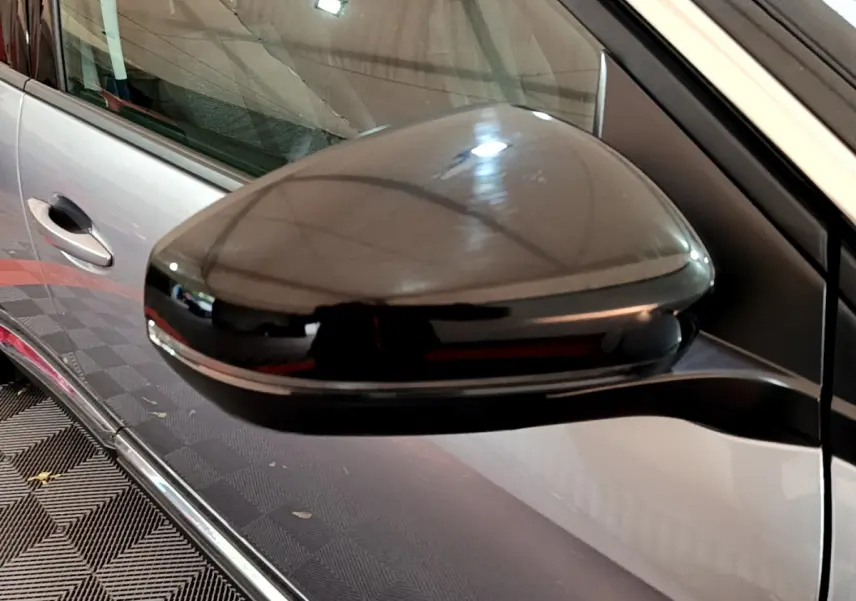 Rétroviseur noir brillant côté gauche d’un Peugeot 5008 gris clair vu de près, avec poignée de porte visible en arrière-plan.