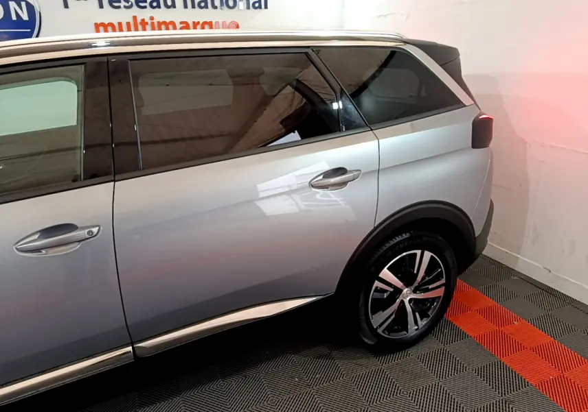Vue côté droit arrière du Peugeot 5008 gris clair avec jante alliage et vitres teintées dans un showroom.