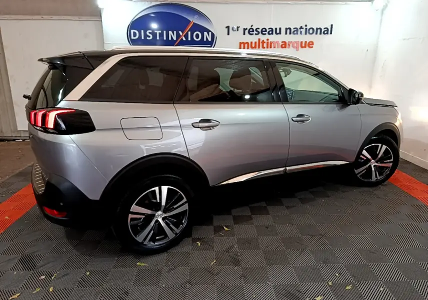 Peugeot 5008 gris clair vue de profil droit en intérieur, avec feux arrière allumés et jantes alliage.