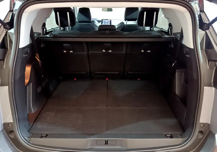 Coffre ouvert vu de l'arrière d'un Peugeot 5008 gris clair, montrant la 3ème rangée de sièges rabattue et plancher plat.
