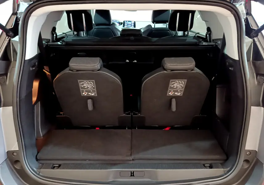 Vue arrière du coffre ouvert d'un Peugeot 5008 gris clair, montrant la 3ème rangée de sièges individuels rabattus.