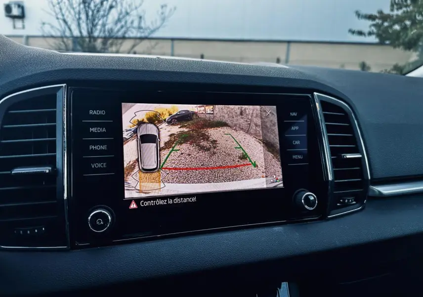 Écran tactile du tableau de bord d’un Skoda Karoq blanc 2024 montrant la caméra de recul avec guidage au stationnement.