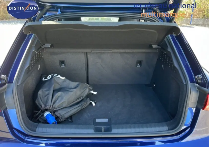 Coffre ouvert vu de l'arrière d'une Audi A3 Sportback bleu Navarre métal avec sac noir à l'intérieur.