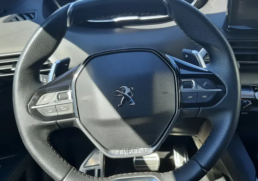 Vue rapprochée du volant cuir noir perforé du Peugeot 3008 GT avec logo lion et commandes intégrées.