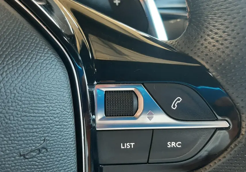 Gros plan sur les commandes gauche du volant noir perforé du Peugeot 3008 2023, avec molette et boutons fonction audio.