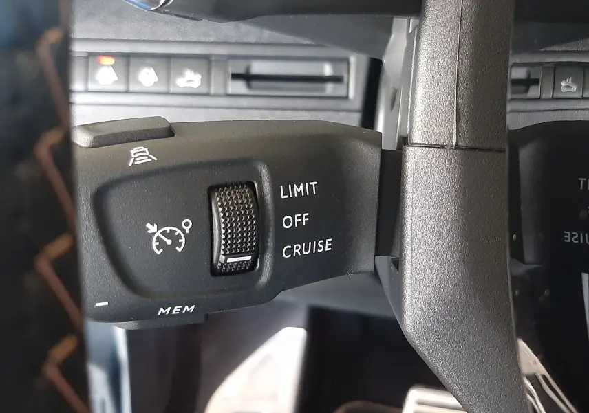 Gros plan sur la commande de régulateur de vitesse à gauche du volant dans l’habitacle noir du Peugeot 3008 2023.