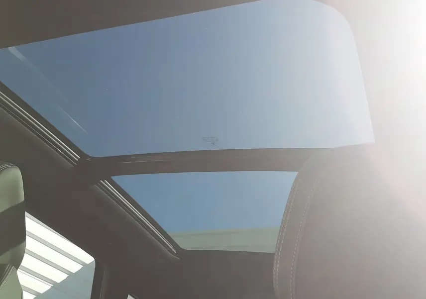 Vue intérieure du toit panoramique en verre du Peugeot 3008 GT 2023, avec ciel bleu visible et sièges noirs.