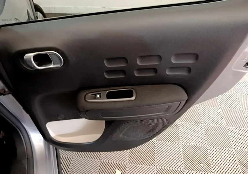 Vue rapprochée de la porte côté gauche gris clair de la Citroën C3 avec poignée argentée et panneau noir texturé.