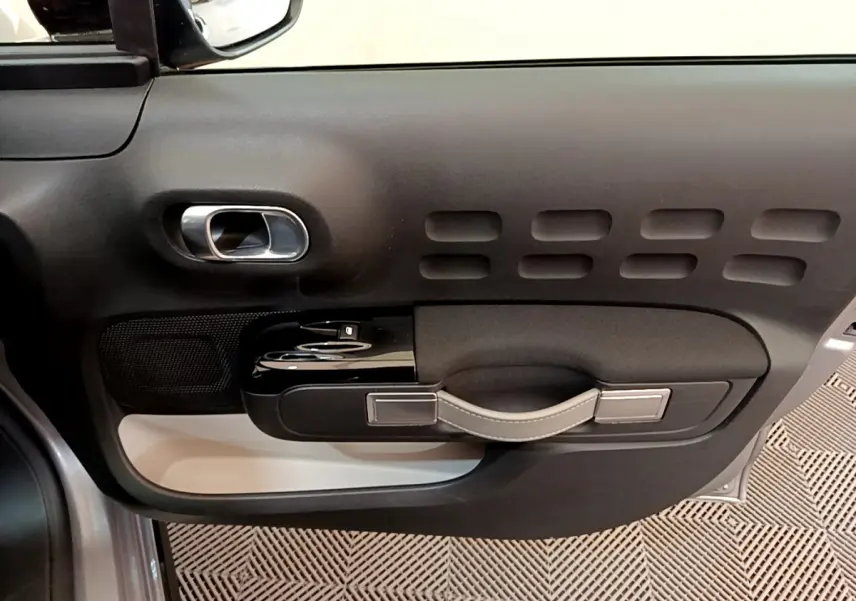 Vue rapprochée de la porte côté conducteur de la Citroën C3 gris clair, montrant la poignée et les commandes de fenêtre.