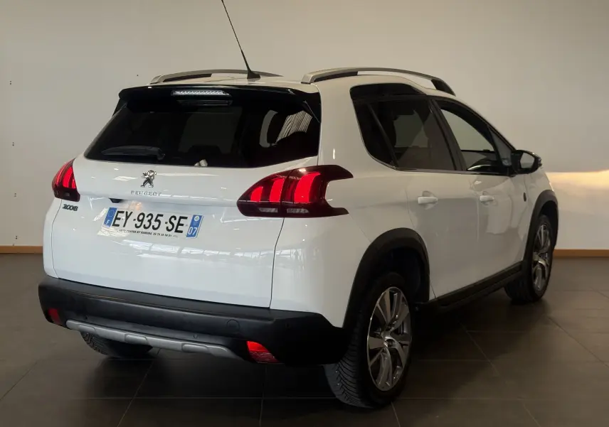 Peugeot 2008 blanc vue 3/4 arrière droit, avec barres de toit et feux arrière allumés en intérieur.