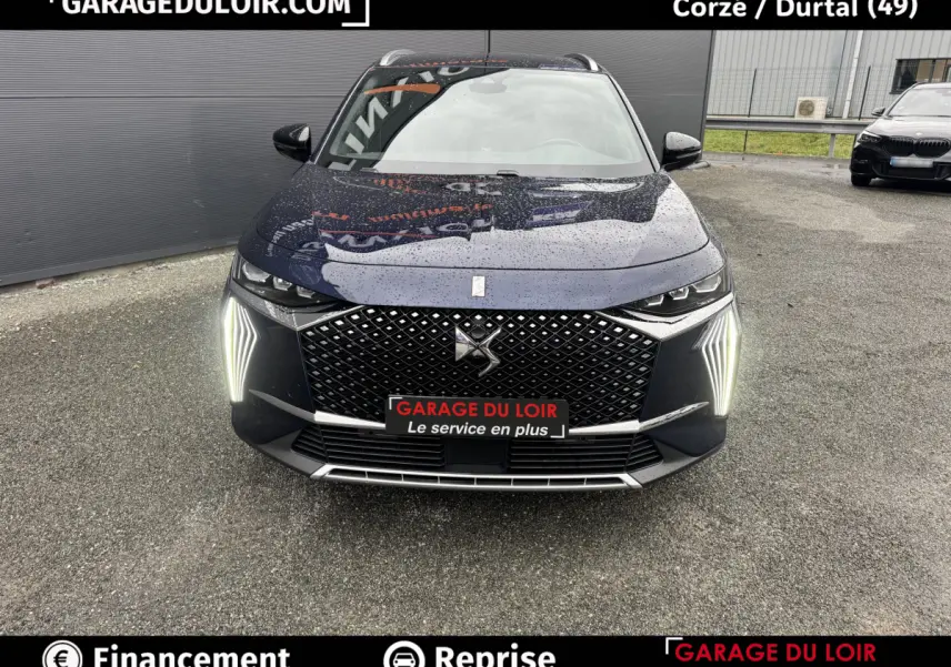 Vue avant d'un DS7 Crossback bleu avec calandre diamantée et feux LED verticaux allumés sur parking.