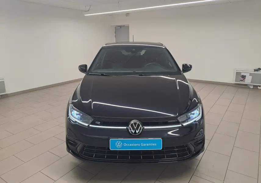 Vue avant d'une Volkswagen Polo 1.0 TSI R-Line noire intense avec phares allumés en intérieur showroom.