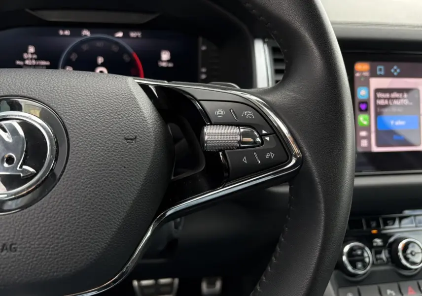Gros plan sur la partie droite du volant noir du Skoda Kodiaq 2024 avec commandes intégrées et tableau de bord numérique en arrière-plan.