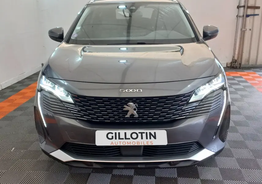 Vue frontale d'un Peugeot 5008 gris foncé avec phares LED allumés et calandre noire distinctive.