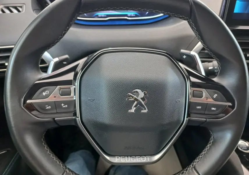 Volant cuir noir de Peugeot 5008 2021 avec commandes multifonctions et logo lion au centre, vue de face rapprochée.