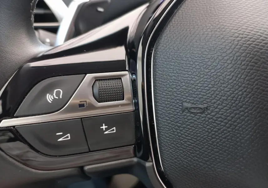 Gros plan sur les commandes vocales et volume du volant cuir noir du Peugeot 5008 gris foncé, version 2021 Allure Pack.