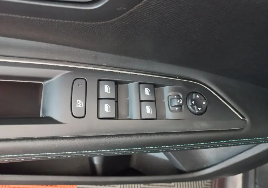 Gros plan sur la commande des vitres et rétroviseurs côté conducteur du Peugeot 5008 gris foncé, avec surpiqûres bleues.