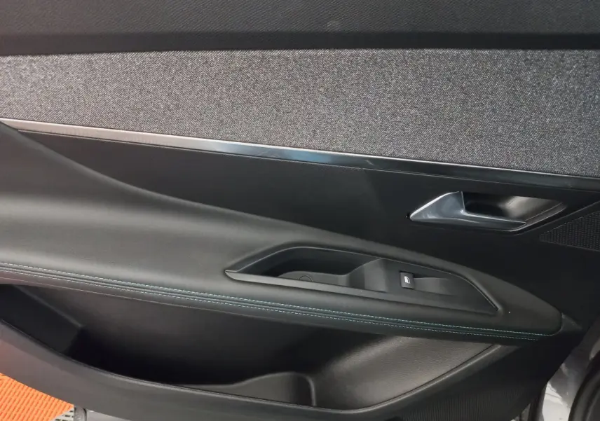 Gros plan sur la porte intérieure côté gauche du Peugeot 5008 gris foncé, avec poignée et bouton de vitre électrique.