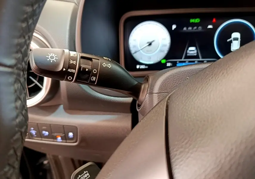 Vue intérieure centrée sur le volant cuir et la commande des feux, avec tableau de bord numérique du Hyundai Kona bleu 2023.