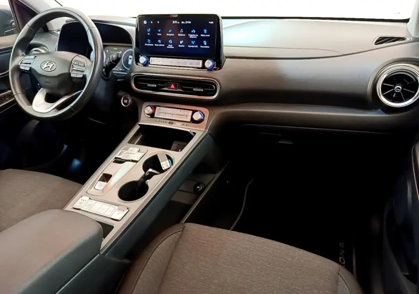 Vue intérieure avant droite du Hyundai Kona électrique 2023, tableau de bord noir avec écran tactile central et volant cuir multifonctions.