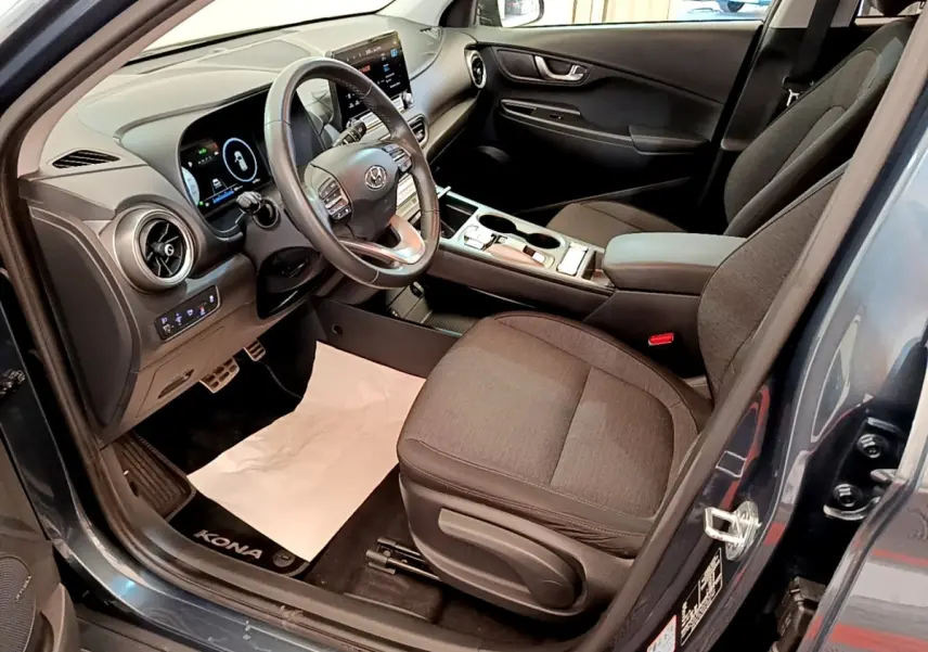 Vue intérieure côté conducteur du Hyundai Kona électrique 2023 bleu, avec volant cuir multifonctions et tableau de bord digital.