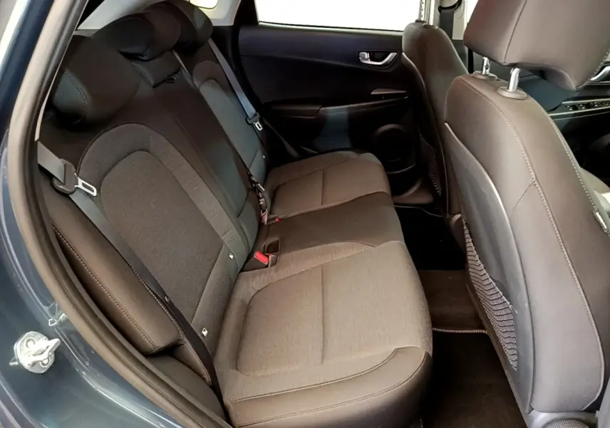 Vue intérieure côté arrière gauche du Hyundai Kona électrique 2023, montrant la banquette arrière en tissu gris et noir.