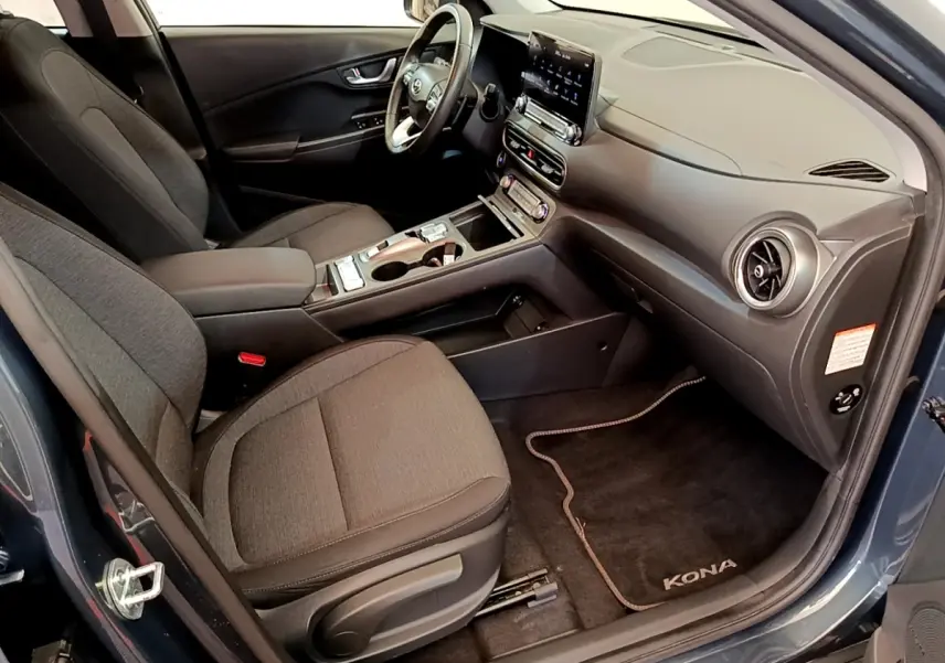 Vue intérieure côté conducteur de la Hyundai Kona électrique 2023 bleu, avec volant cuir multifonctions et tableau de bord moderne.