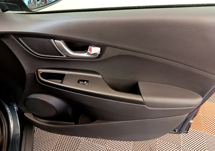 Vue rapprochée de la porte intérieure côté gauche bleu foncé du Hyundai Kona électrique avec poignée argentée et haut-parleur intégré.