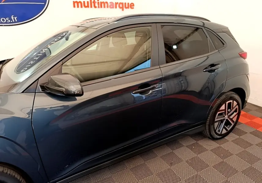 Vue latérale gauche d’un Hyundai Kona électrique bleu avec jantes distinctives et rétroviseurs noirs rabattables.