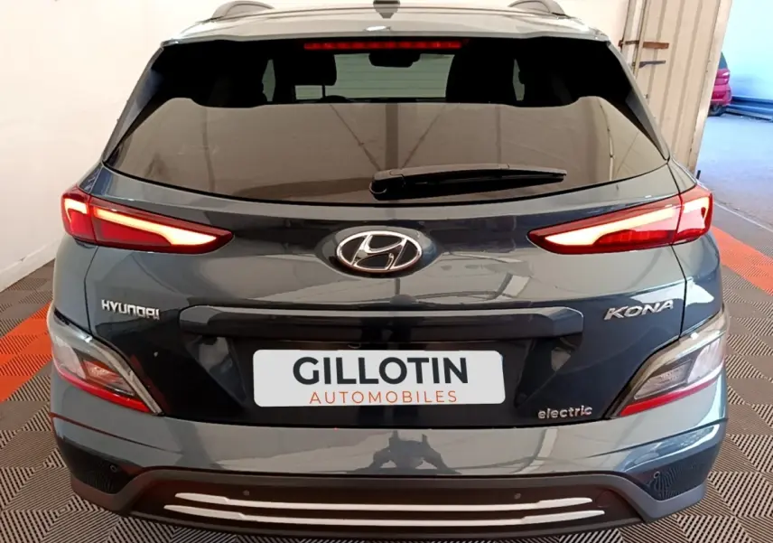 Vue arrière d'un Hyundai Kona électrique bleu avec feux LED allumés et logo visible sur un sol à damier rouge et noir.