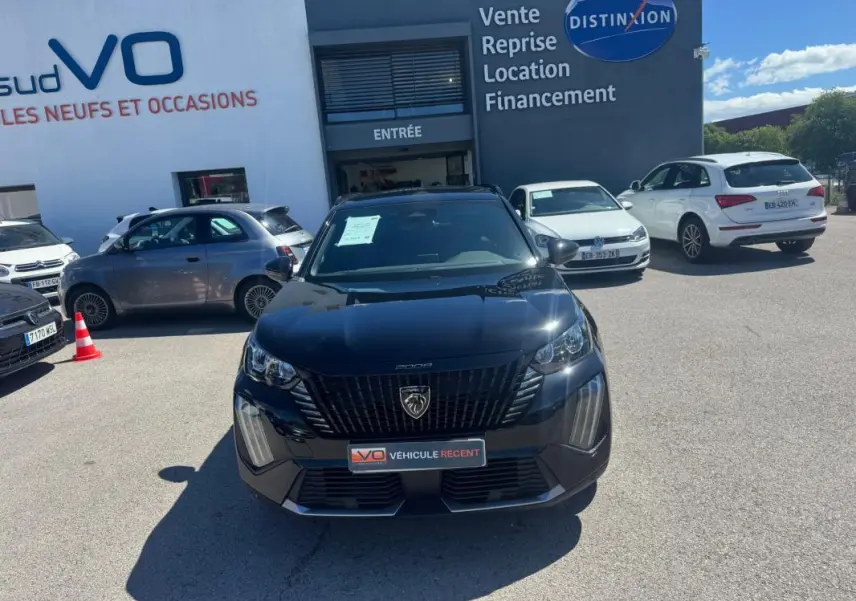 Vue avant d’un Peugeot 2008 Hybrid noir 2025 avec pack hiver, stationné devant un concessionnaire automobile.